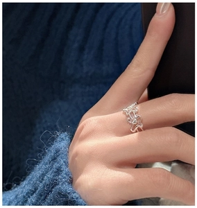 Gros plan d'une bague fleur ajourée en argent S925 portée au doigt sur fond de pull bleu