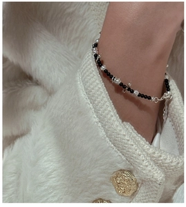 Detail of beaded bracelet with black polished beads and silver cross pendant on wrist