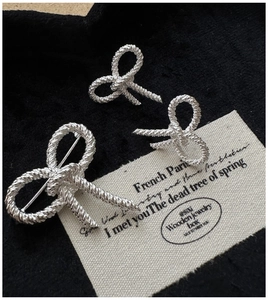 Detail view of silver bow earrings and brooch with twisted rope texture on a dark fabric