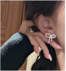 Detail of twisted silver bow stud earring on model's ear showing realistic texture
