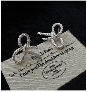 Detailed view of S925 sterling silver twist bow earrings with woven texture on a fabric base