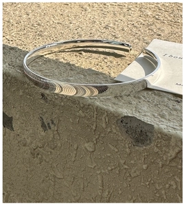 Detail eines polierten S925 Silberarmreifs auf einem Sockel aus Naturstein