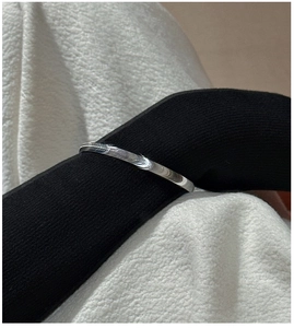 Nahaufnahme eines minimalistischen Silberarmreifs über einem schwarzen Strickärmel