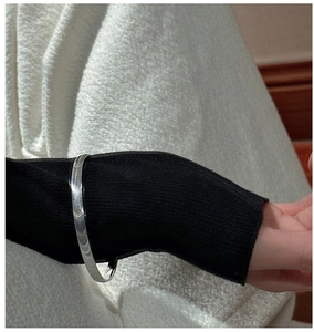 Minimalistisches S925 Silberarmband über schwarzem Strickärmel gestylt für einen trendigen Look