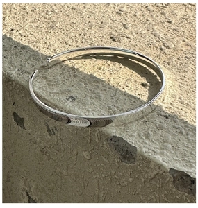 Nahaufnahme eines minimalistischen S925 Silberarmreifs mit strukturierten Kanten auf Stein