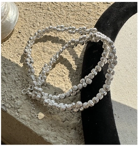 Detail of silver beaded necklace with diamond-cut texture and heart charm on gray stone