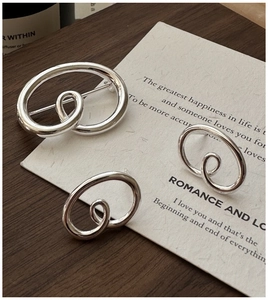 Macro view of minimalist S925 silver pretzel-shaped brooch and matching stud earrings
