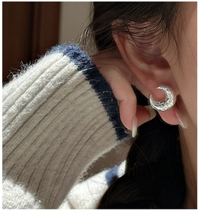 Macro shot of silver crescent earrings with artistic lava texture worn by a model