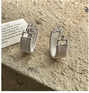 Macro shot of silver wire-wrapped square hoop earrings on a textured stone surface