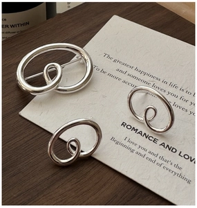 Macro shot of silver knot earrings and brooch set on textured paper and wood