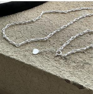 Dettaglio macro della catena d'argento a maglie ritorte con chiusura a moschettone e tag