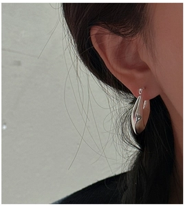 Macro detail of polished silver teardrop hoop earrings on model with glossy finish