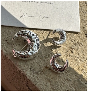 Detailed close-up of textured moon-shaped silver earrings and brooch set on stone
