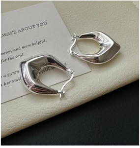 Detailed macro view of S925 sterling silver shield-shaped earrings on a cream leather surface