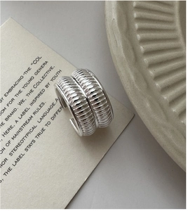 Detailed view of C-shaped silver earrings with vertical ribbed texture on white card