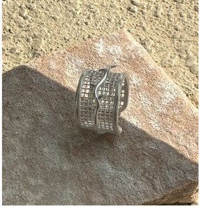 Macro shot of silver woven mesh ring with wave detail on a natural stone surface