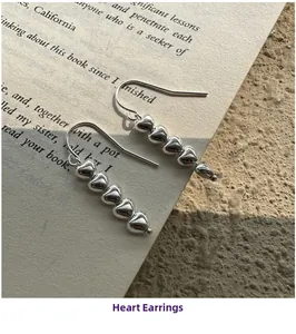 Macro detail of silver heart drop earrings vertically linked on a printed book page