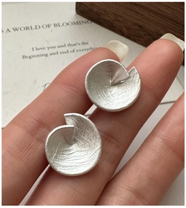 Gros plan de boucles d'oreilles en argent avec texture métal brossé et disque spirale