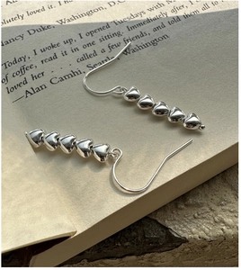 Detail of silver S925 heart drop earrings featuring five linked charms on a book