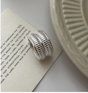 Detailed close-up of wide silver band ring with vertical corrugated texture on card