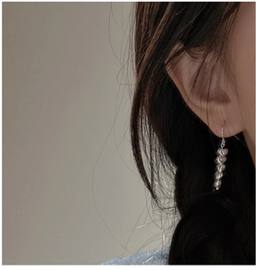 Detailed view of sterling silver heart drop earrings worn on ear with polished finish