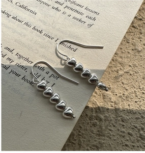Close-up of S925 silver heart drop earrings placed on a book with soft shadows