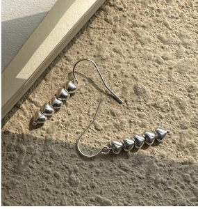 Macro detail of five linked silver heart drop earrings on a textured stone surface