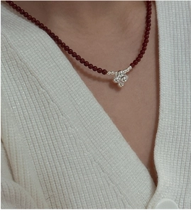 Detailed view of deep red beaded necklace with silver spherical pendant on white knit
