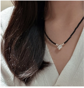 Close-up of black beaded necklace with a silver 3D flower pendant on a model