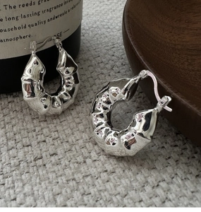 Détail des boucles d'oreilles créoles en argent S925 avec texture plissée sur du tissu