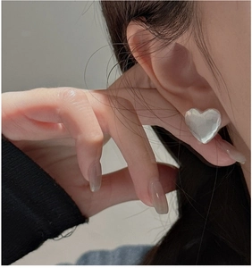 Detail view of heart stud earrings with marble texture on ear of woman