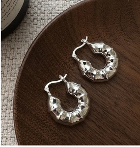 Détail macro de boucles d'oreilles argentées texturées sur plateau bois et lin