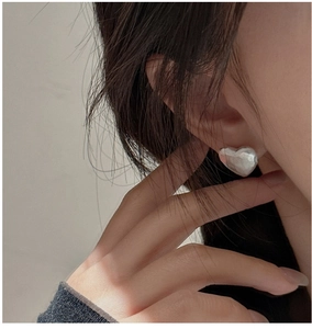 Detail shot of silver heart stud earrings with hammered texture on a model's ear