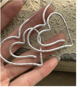 Detailed view of silver heart earrings with vintage matte texture held in hand