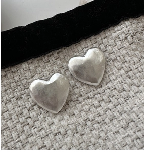 Macro shot of matte S925 sterling silver heart studs with brushed texture on tweed cloth