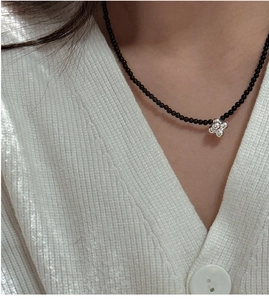 Close-up of black beaded necklace with silver flower pendant on a female model