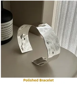 Close-up of a wide silver cuff bracelet with unique wavy texture on a minimalist stone base