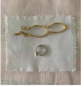 Close-up of S925 sterling silver square ring and wavy gold bracelet on rustic linen fabric