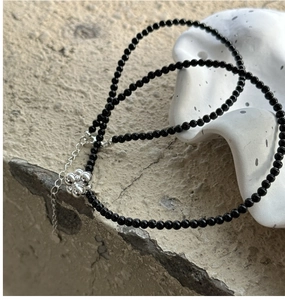 Close-up of black onyx beaded necklace featuring a silver floral cluster pendant on stone
