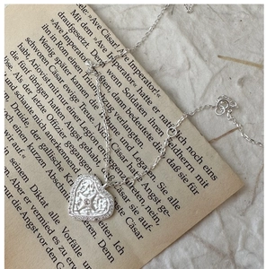 Macro detail of silver heart necklace with starburst diamond on vintage paper
