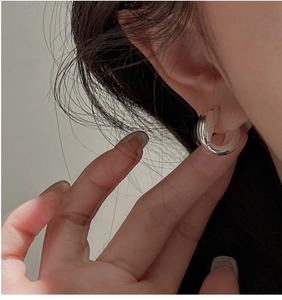 Detail view of U-shaped silver hoop earring on ear with polished metallic finish