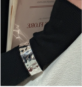Detailed close-up of a wide silver cuff bracelet with unique hammered texture surface