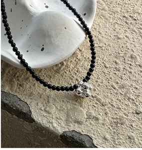 Macro shot of polished silver floral pendant and 4mm black agate beaded necklace on stone