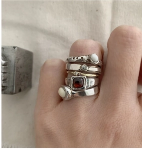 Macro shot of S925 silver stacked rings with opal and ruby stones on textured cloth
