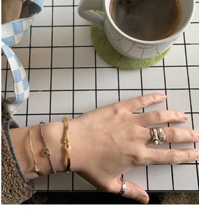 Close-up of stacked silver square rings and heart charm bracelets on woman's hand