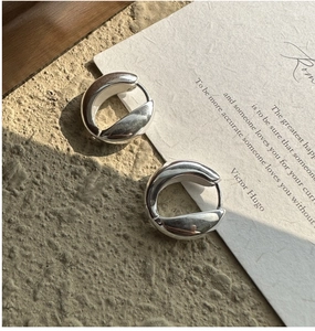 Polished silver U-shaped hoop earrings on sandstone texture with sunlight shadows