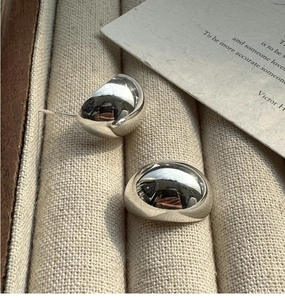 Detailed close-up of bean-shaped S925 silver stud earrings on a textured fabric tray