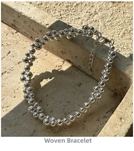 Macro shot of silver beaded woven bracelet with heart charm on textured stone surface