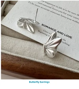 Detail of matte silver butterfly earrings placed on linen jewelry box with elegant card