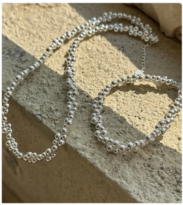 Detail of S925 sterling silver beaded bracelet and necklace set on stone surface
